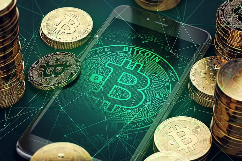 das bitcoin logo digital auf dem handy neben physischen bitcoins