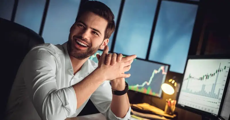lachender trader sitzt vor bildschirmen über dividendenwerte pro aktie