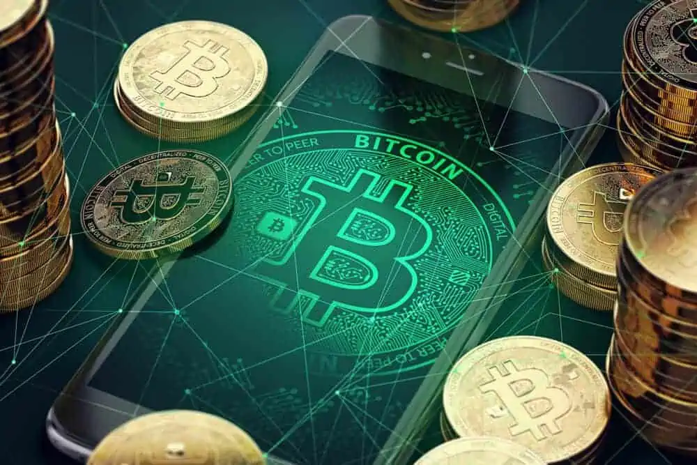 bitcoins als physische münzen als investitionen neben einem handy mit einem digitalen bitcoin